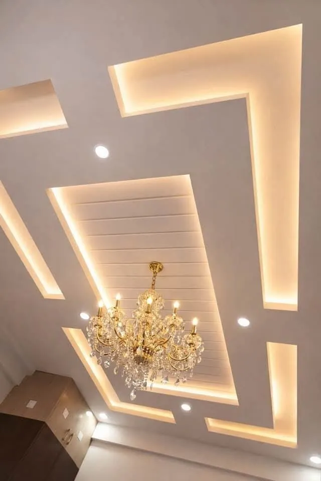 Close view of a layered gypsum ceiling with warm cove lighting and a chandelier